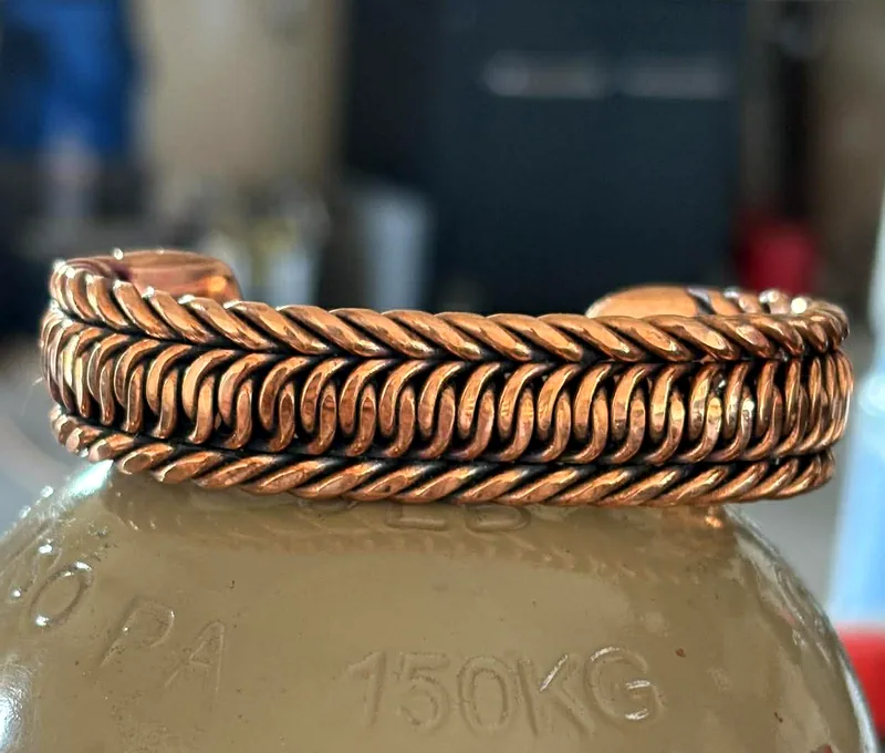 All-copper cuff bracelet woven in the dollar sign pattern with matching copper rope edges.